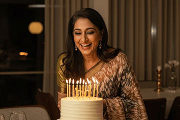 Indian woman celebrating a birthday with a cake and lit candles in a dimly lit room.