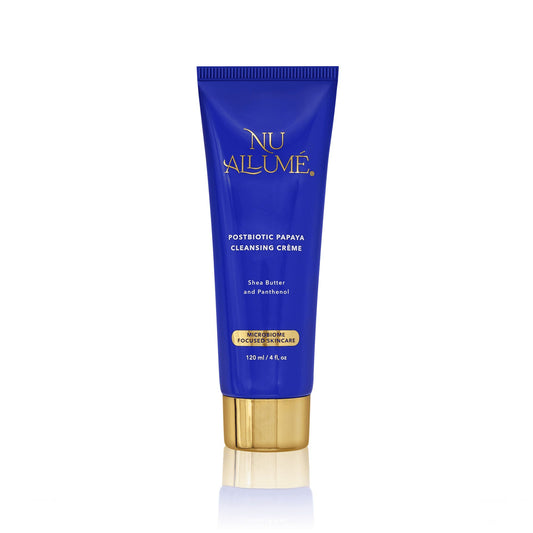 Tube of Nu Allume Postbiotic Papaya Cleansing Crème with gold cap and reflecting below off a white shiny surface