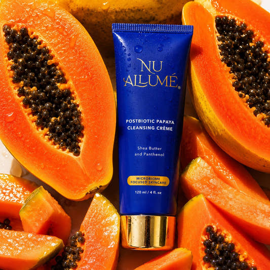 Tube of Nu Allume Postbiotic Papaya Cleansing Crème surrounded by halved papayas.