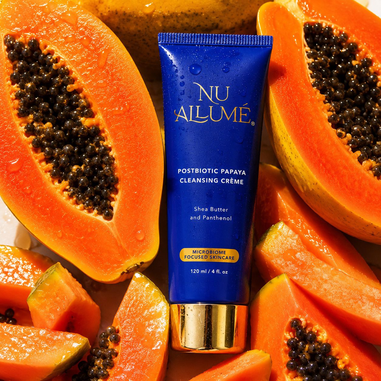 Tube of Nu Allume Postbiotic Papaya Cleansing Crème surrounded by halved papayas.