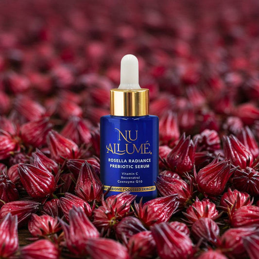 Nu Allumé Rosella Radiance Prebiotic Serum bottle on a background of rosella flowers