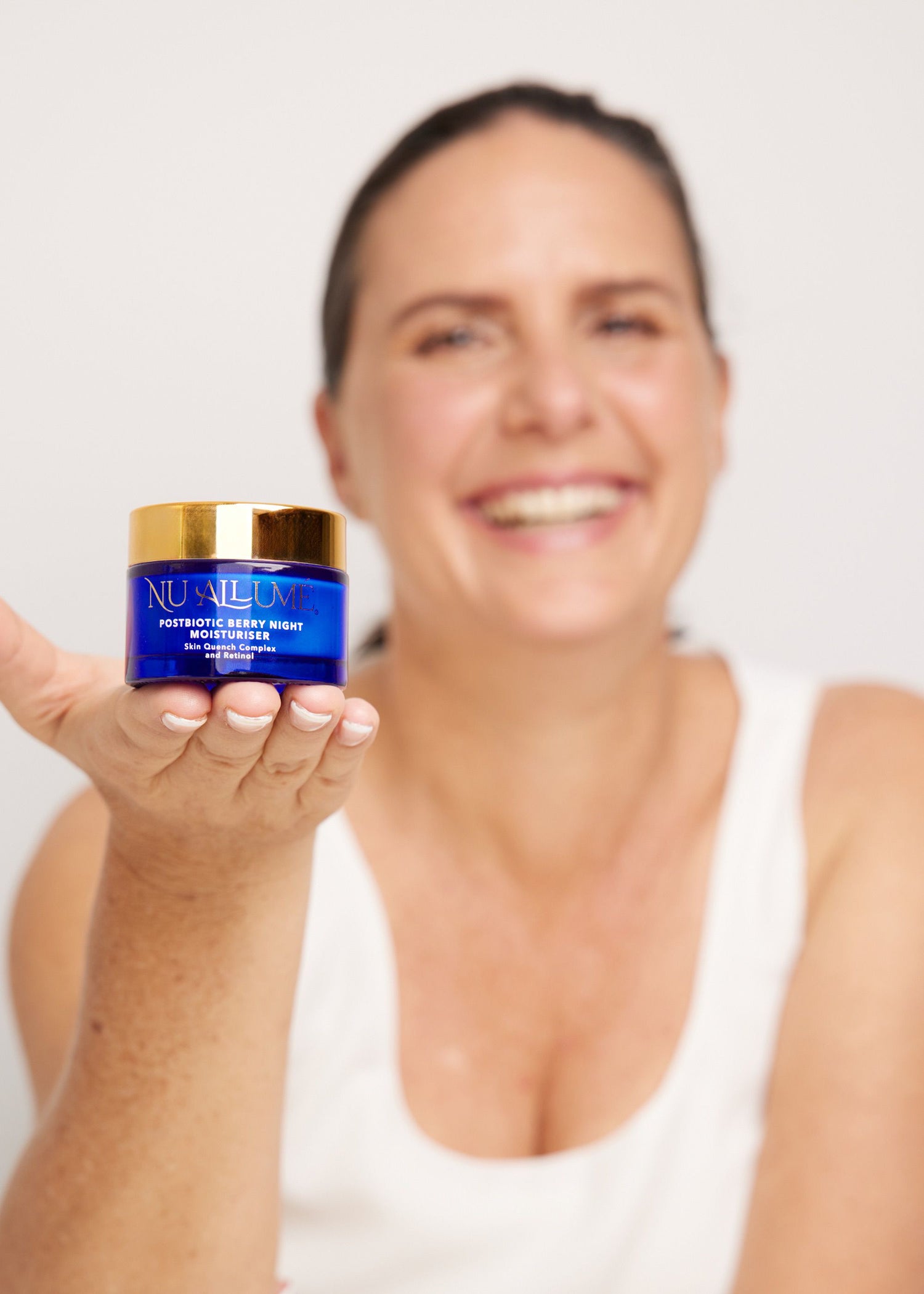 Desre smiling holding a jar of Nu Allume Night moisturiser against a white background