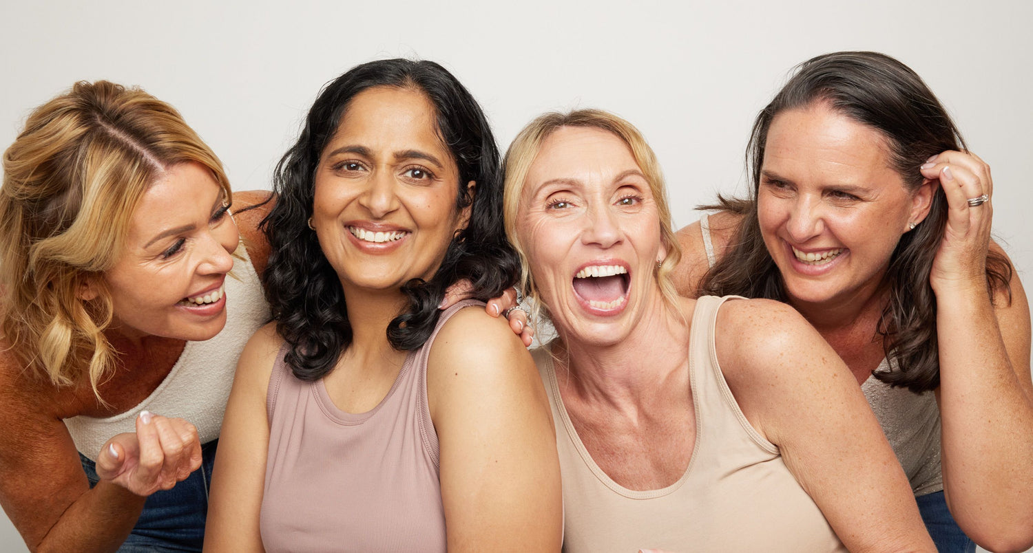 Four women posing together with a plain background all laughing