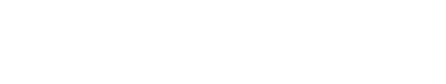 A smiling 60 year old woman in a white dress standing on a beach looking out to sea with mountains in the background.